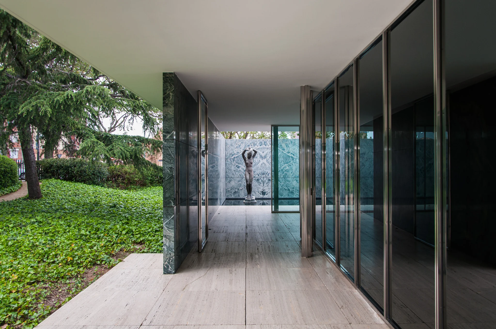A sheltered stone walkway framed by glass, green marble and a planted courtyard.